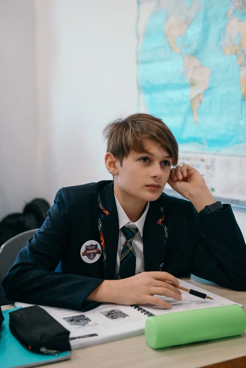 A boy in uniform at his desk with a pencil, a world map behind him