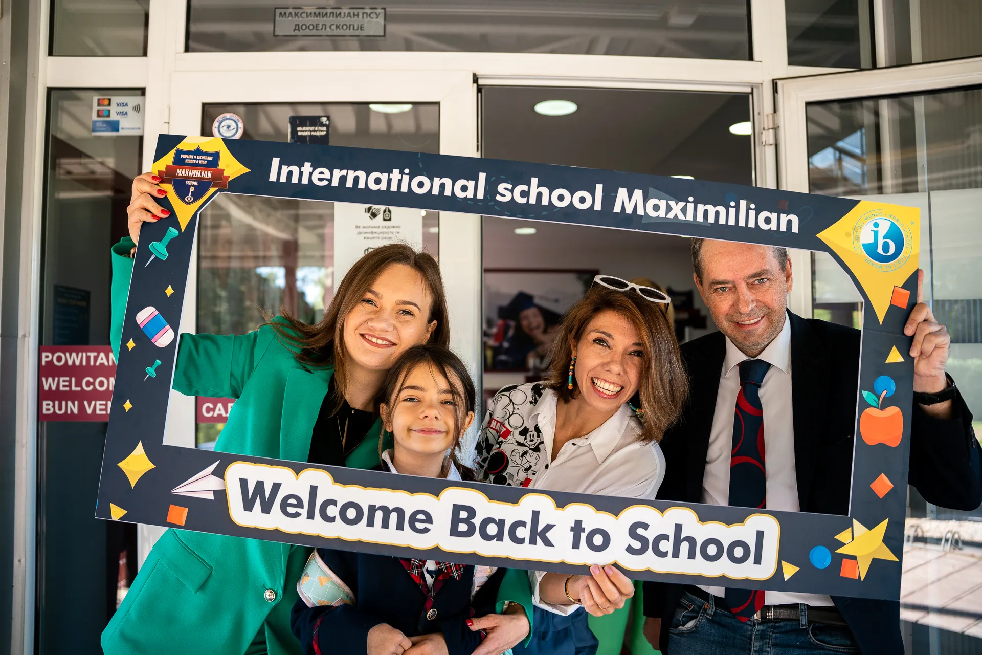 Насмеано семејство држи рамка Welcome Back to School под училишниот влез