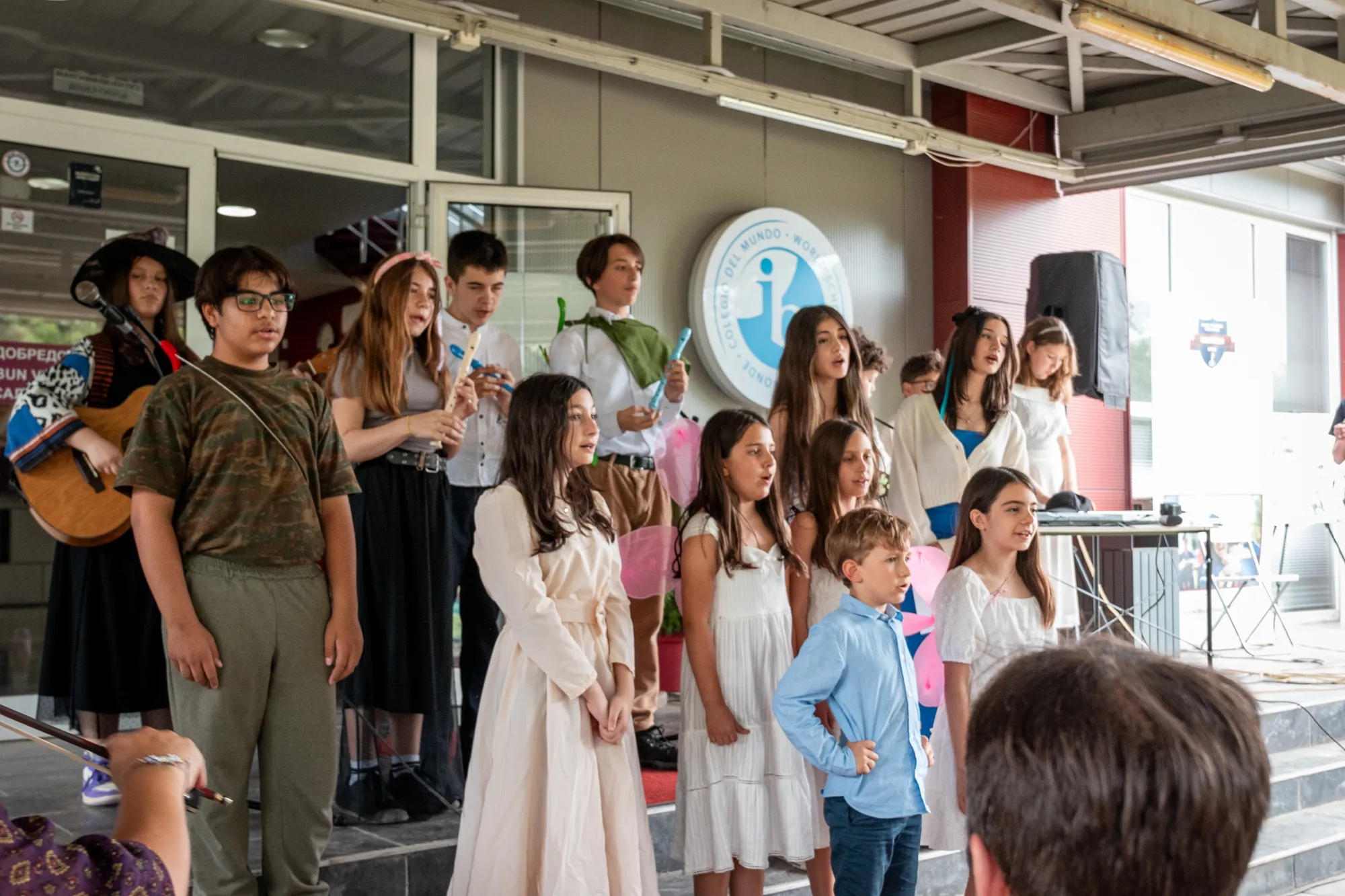 Students performing in costumes at an outdoor school event beneath the IB World School sign