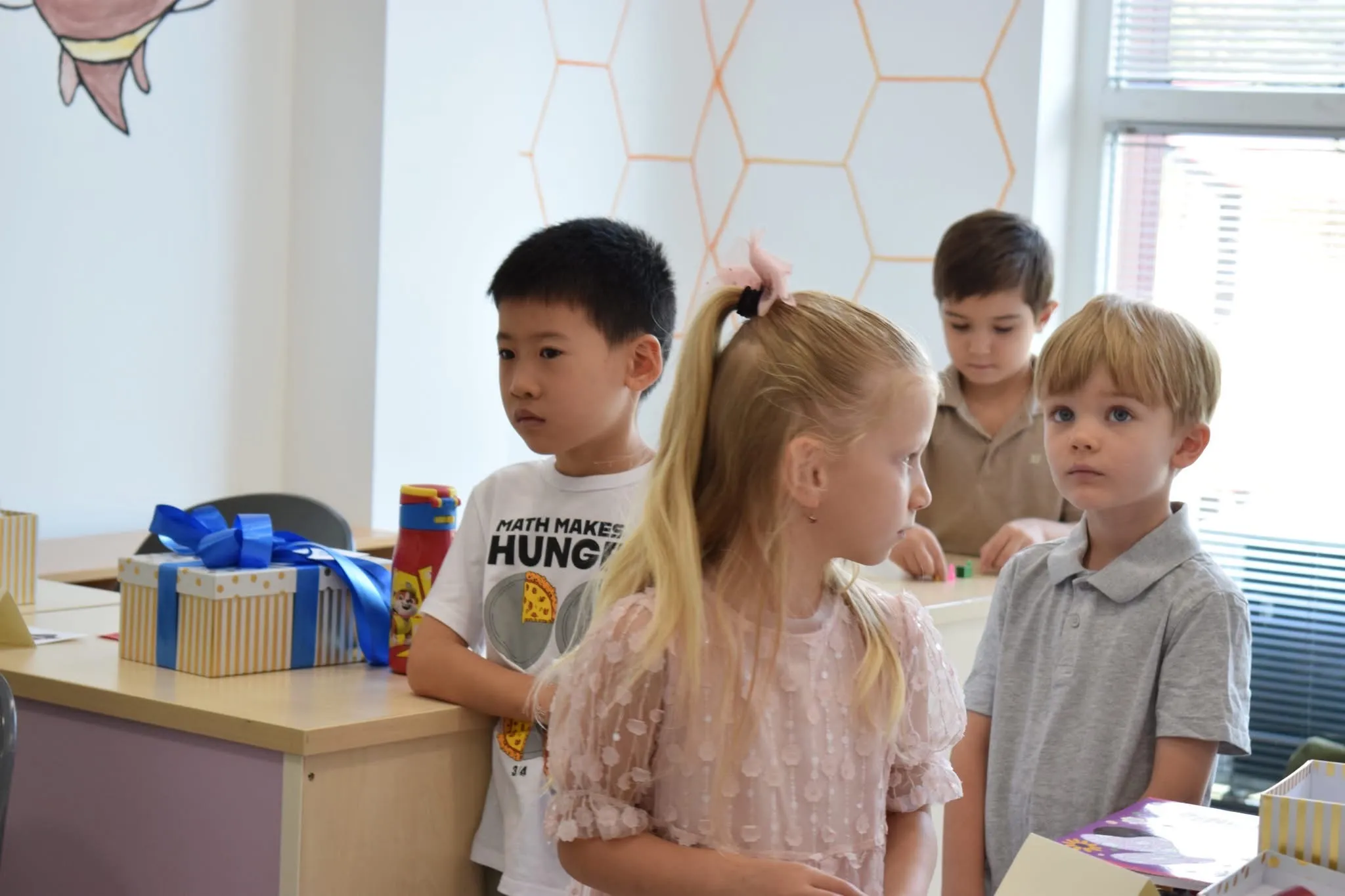 First graders in their best clothes beside wrapped welcome gifts under the honeycomb wall on their first day of school