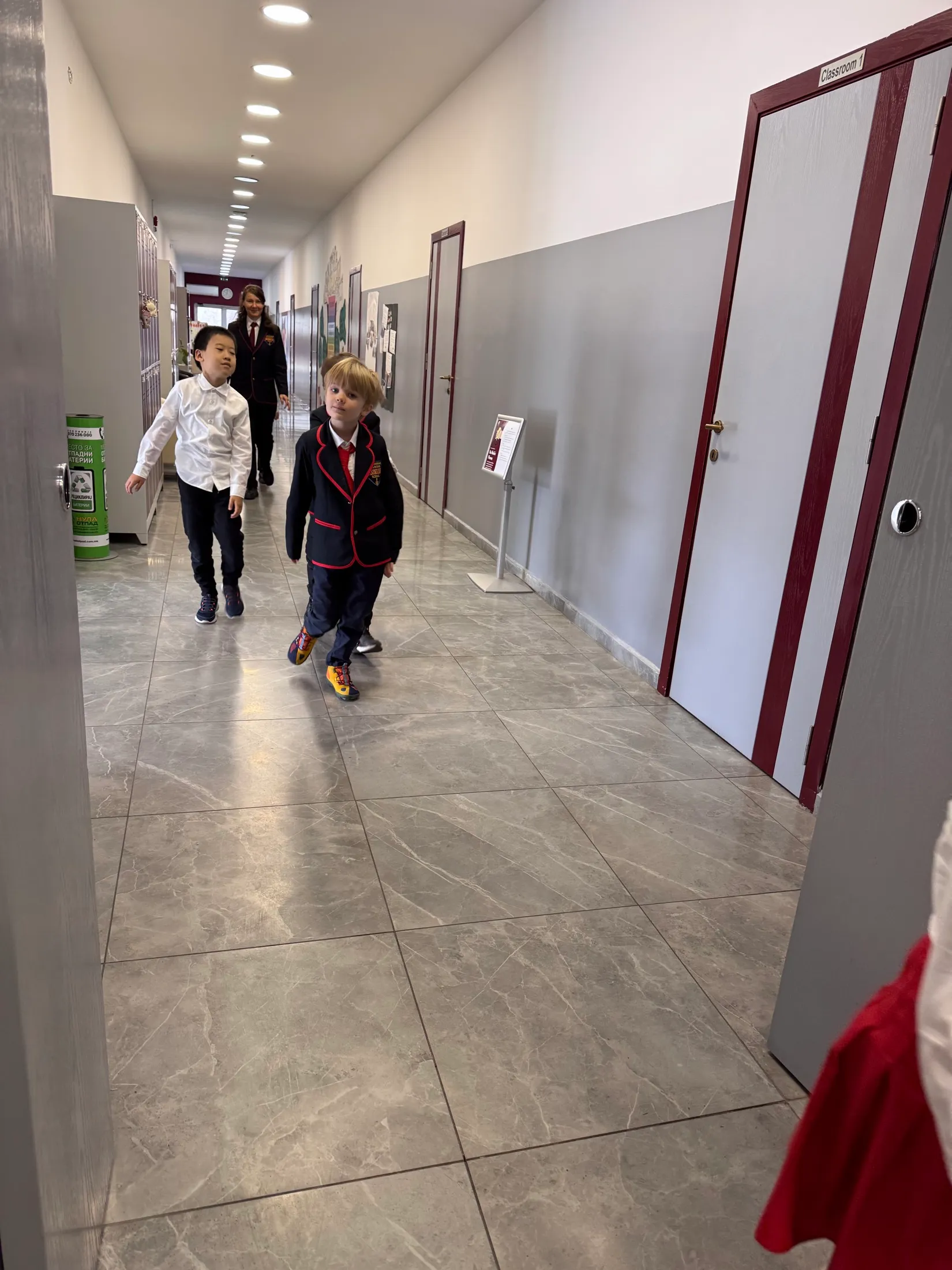 Three first-grade boys in uniform walking down the hallway with their teacher behind them