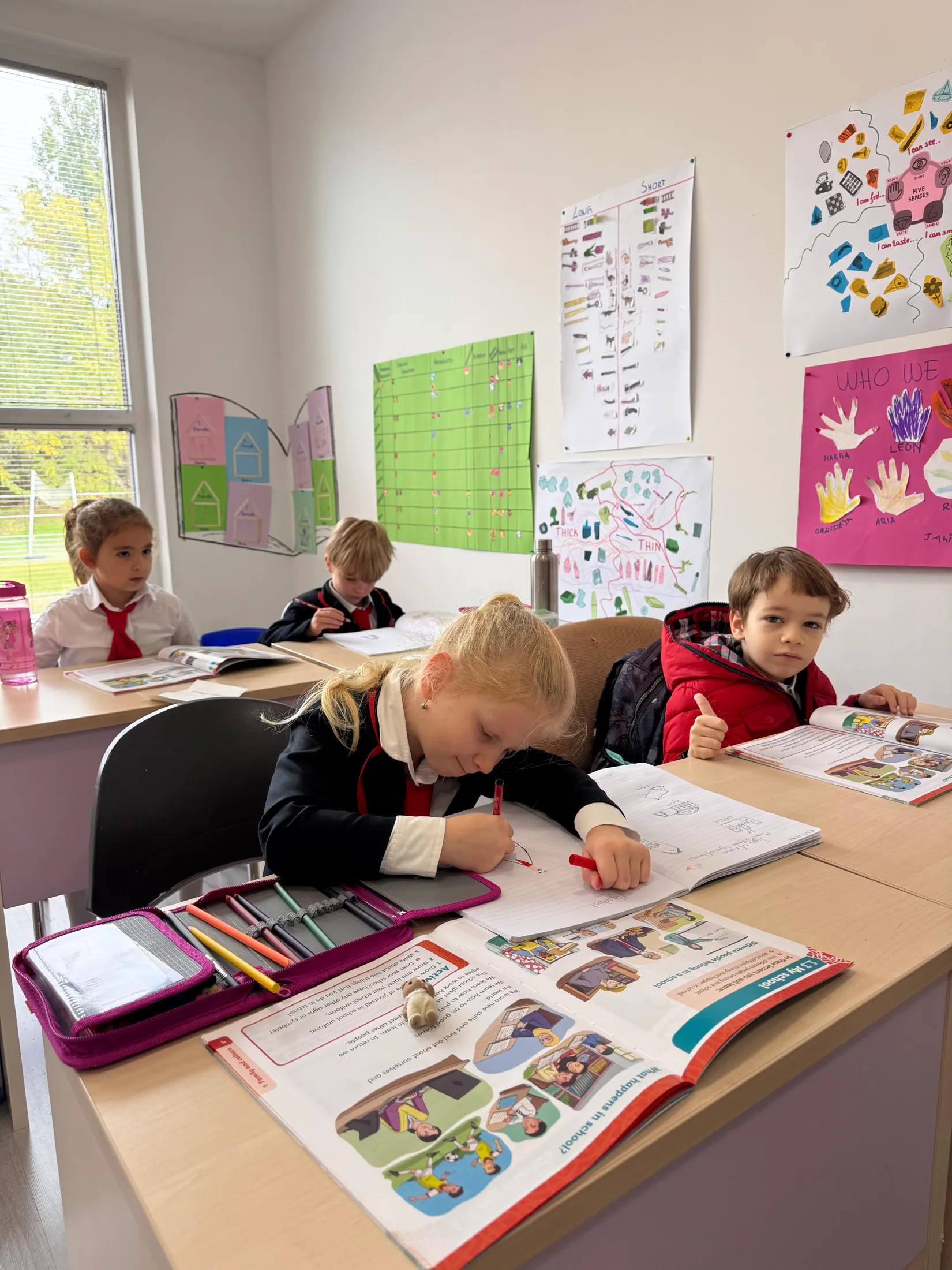 A first grader gives a thumbs up over his workbook while a classmate writes beside him