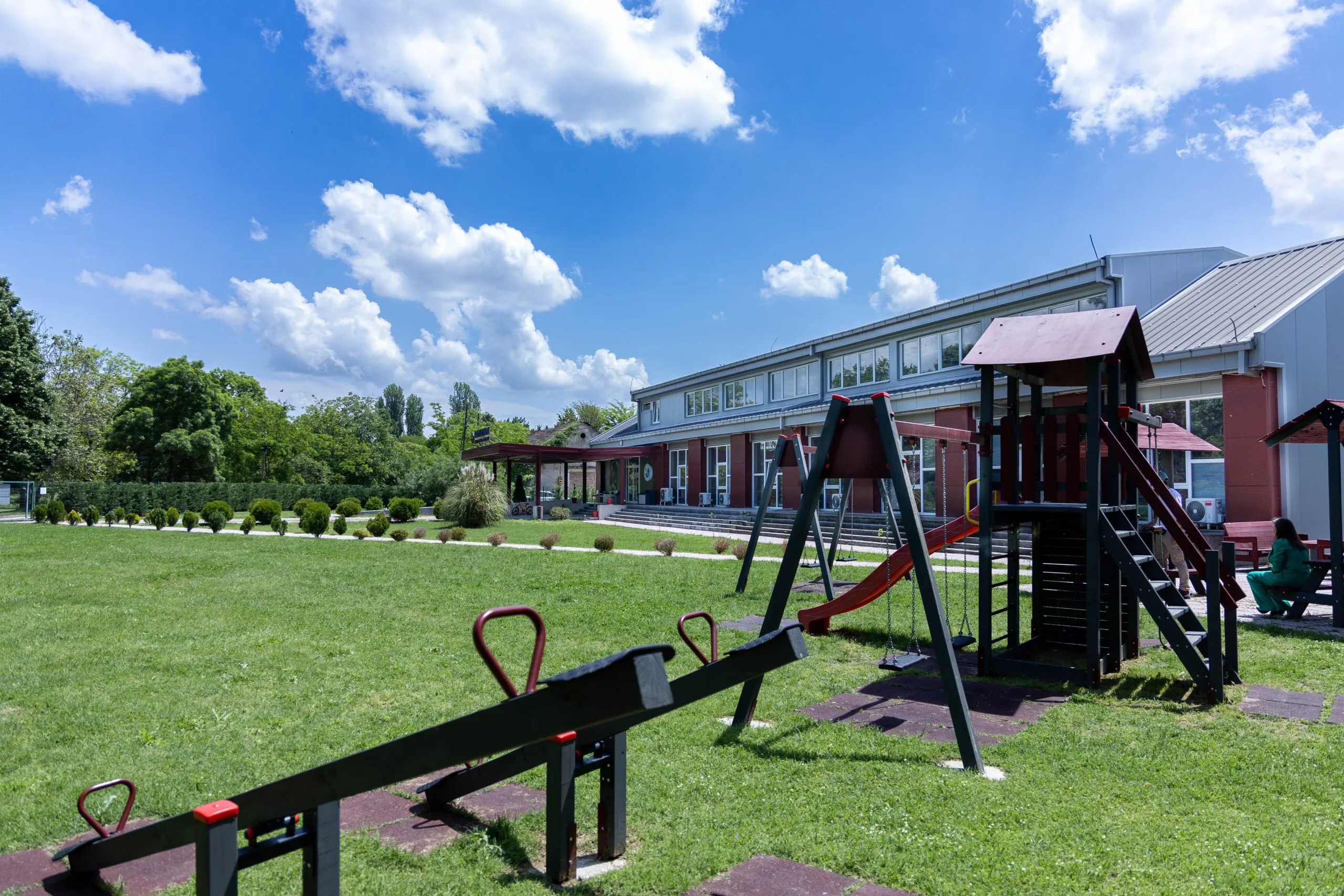 The school building, green lawn, and playground under a vivid blue sky