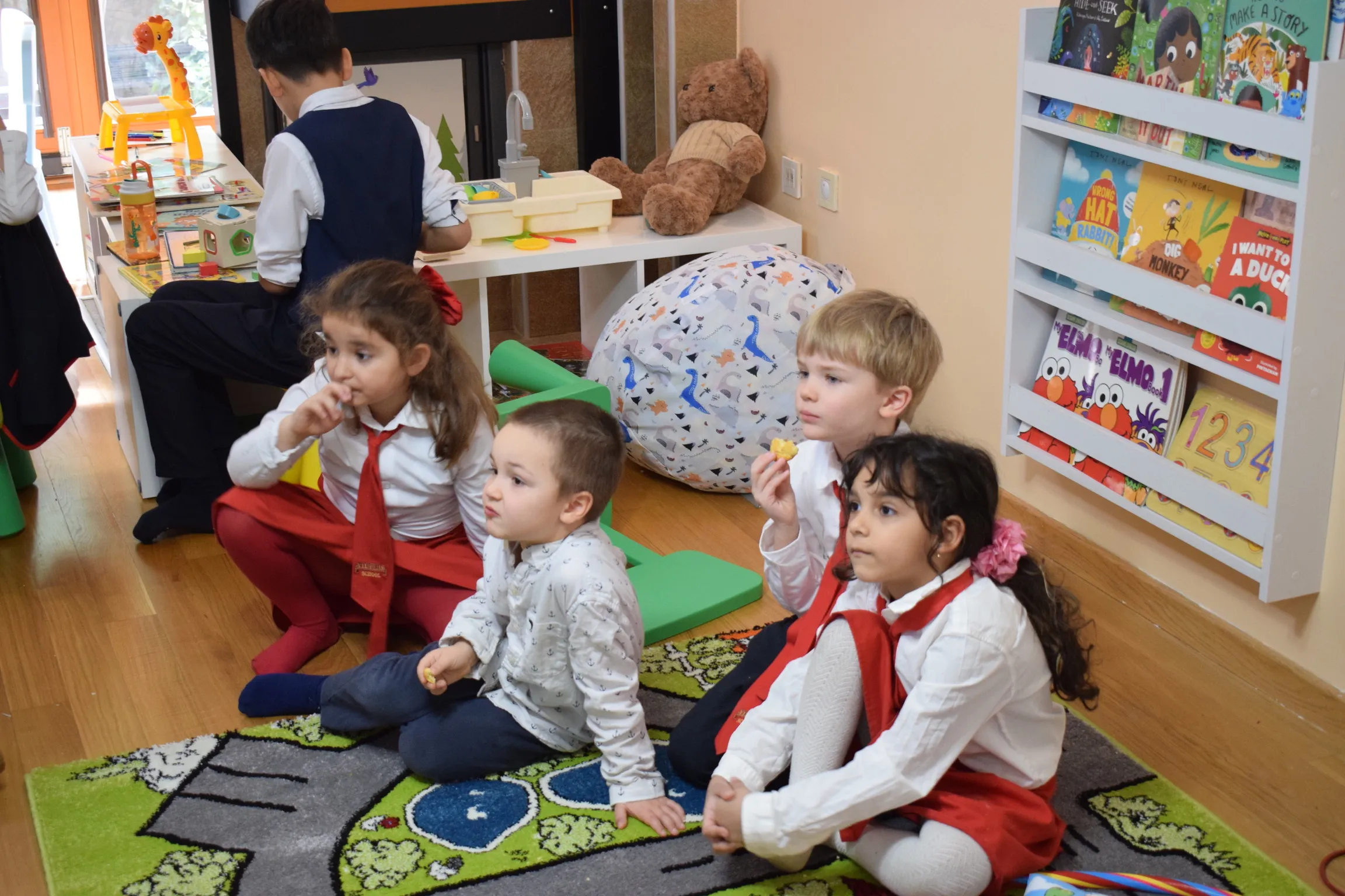 Young children in uniform sitting together on a colourful play rug in the kindergarten